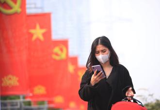 越南薪資節節高升，圖為一名戴著口罩的女性看著手機，行經越南首都河內街頭。（美聯社）
